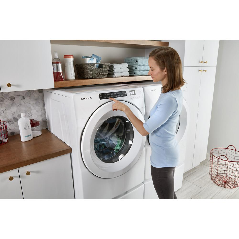 Woman using a white front load washing machine elevated on a white laundry pedestal in a modern appliance setting