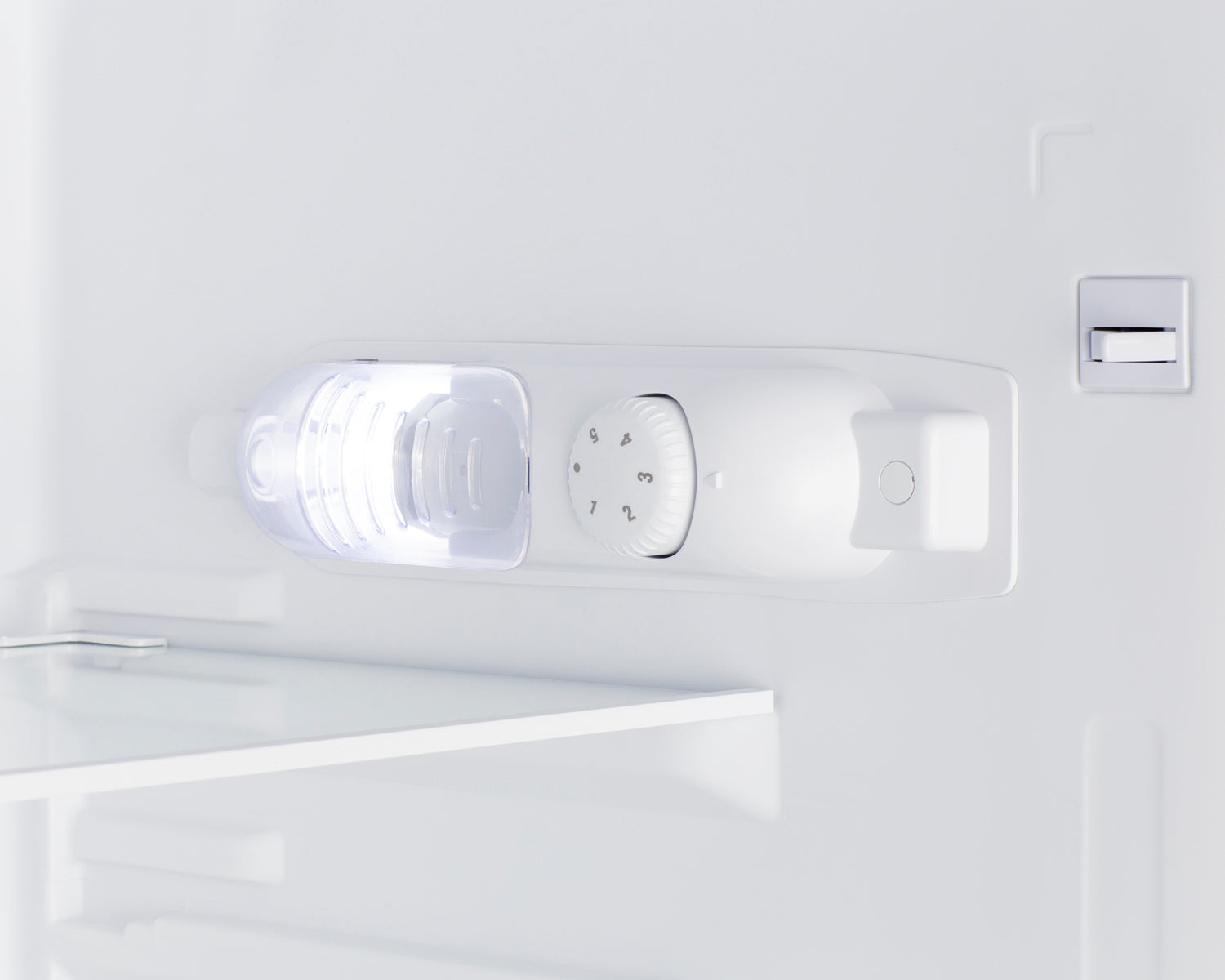 Interior view of white refrigerator with illuminated adjustable temperature control dial and shelf edge visible