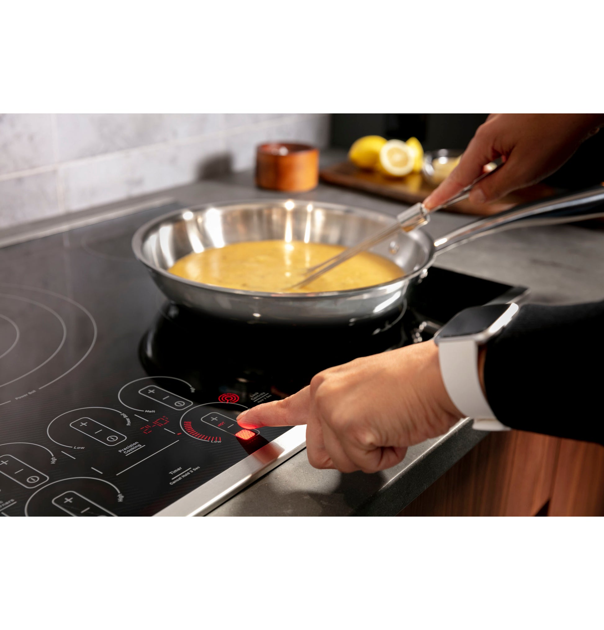 User activating touch control on black electric cooktop while stirring eggs in stainless skillet in modern kitchen