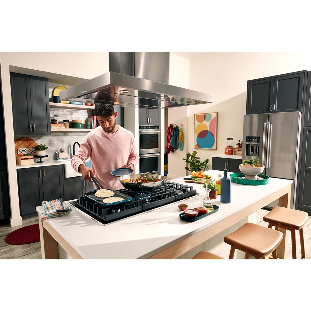 Man cooking on a black 36-inch gas-on-glass cooktop with five burners in a modern kitchen setting for home improvement.