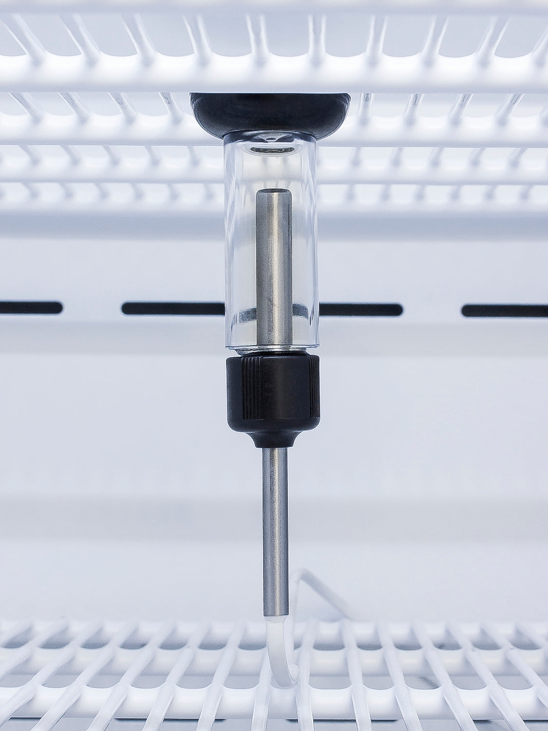 Close-up of stainless steel temperature sensor housed inside clear casing mounted on white wire shelving of upright freezer