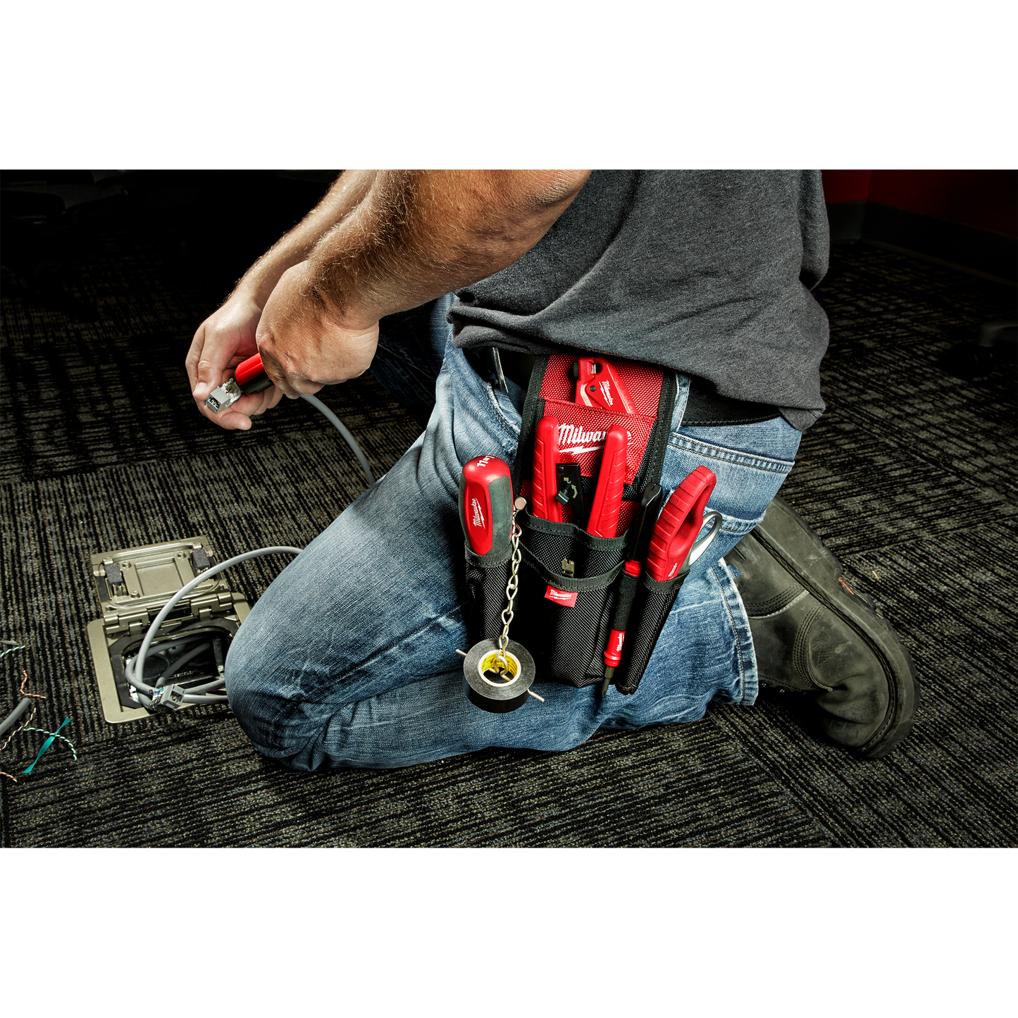 Black and red utility pouch attached to belt holding hand tools and electrical tape for tools and home improvement use