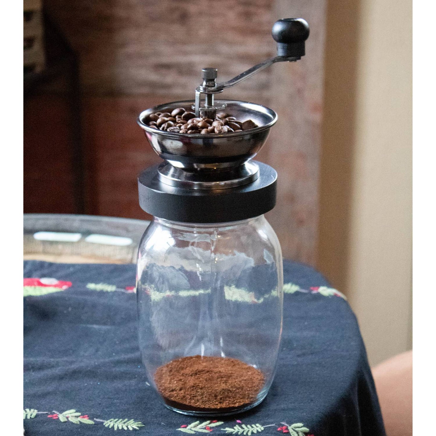 Manual coffee grinder with glass jar and metal bowl filled with coffee beans, part of kitchen gadgets under $50 collection