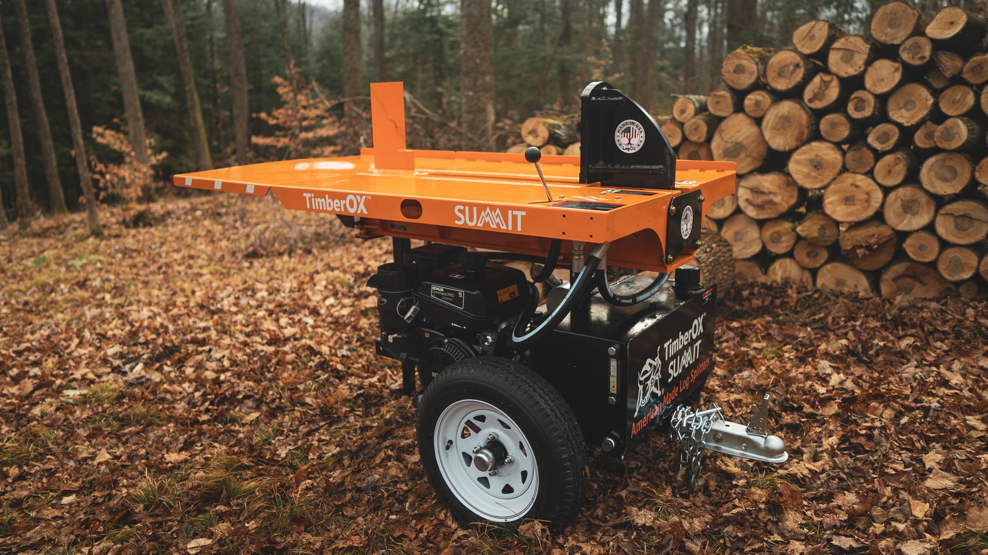 Orange and black log splitter with white wheels positioned near stacked firewood in forest for outdoor wood cutting tasks