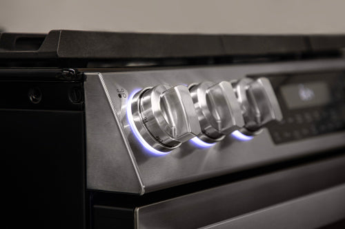 Close-up of stainless steel gas range control knobs with blue LED backlighting in modern kitchen appliances collection