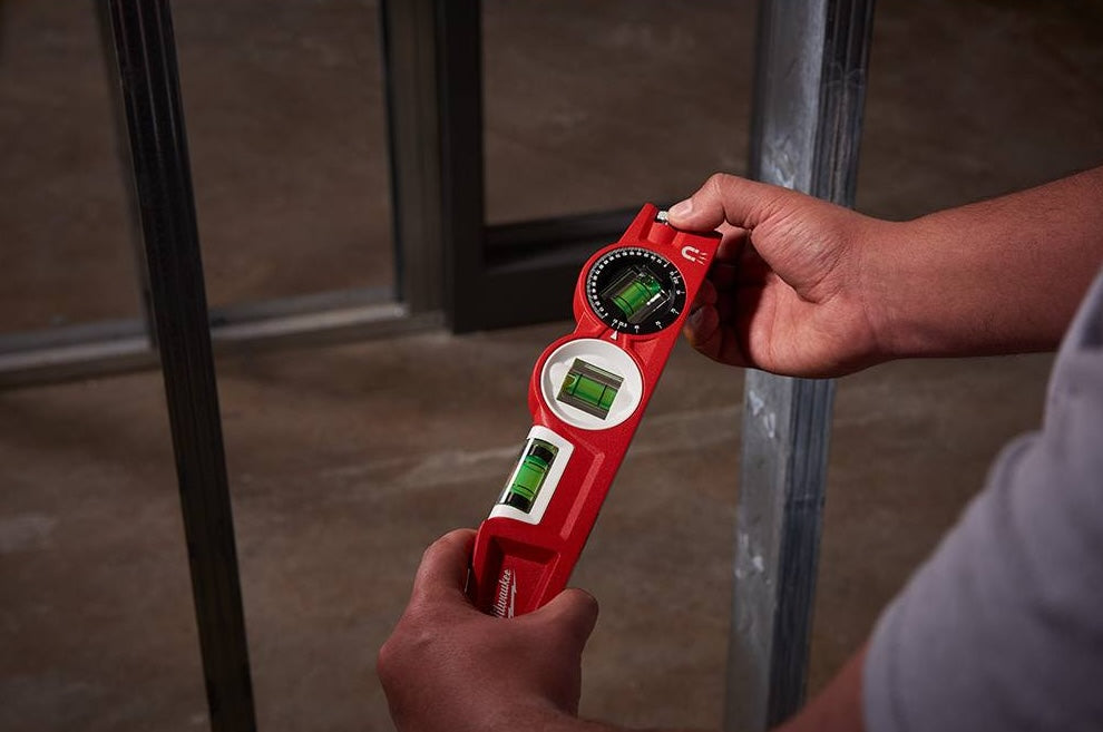 Person holding red torpedo level with 360-degree adjustable vial for precise measurements in woodworking tools collection