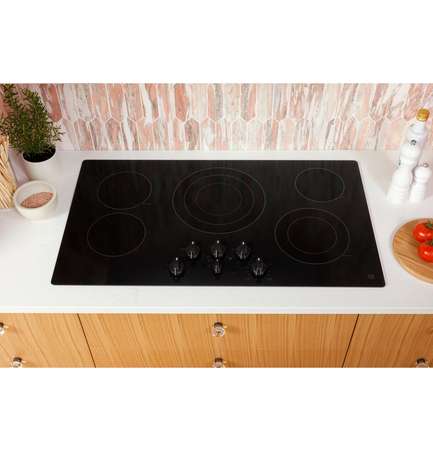 Black smooth built-in electric cooktop with five knob controls on white countertop in modern kitchen setting