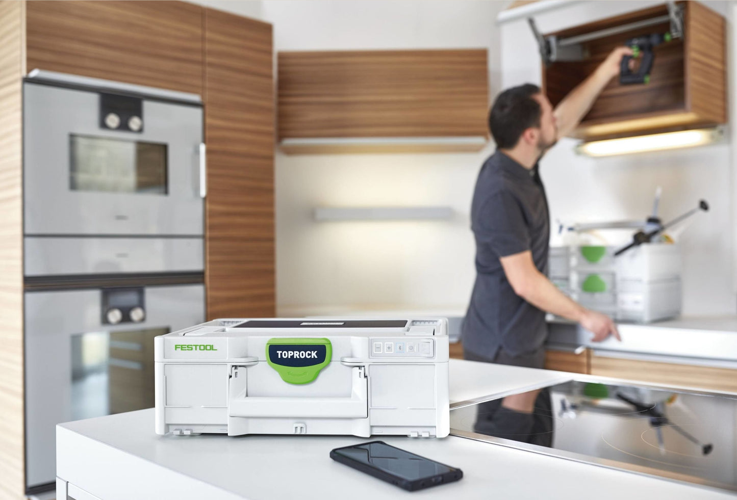 Portable Festool Bluetooth speaker in white and green on kitchen counter with man organizing tools in background