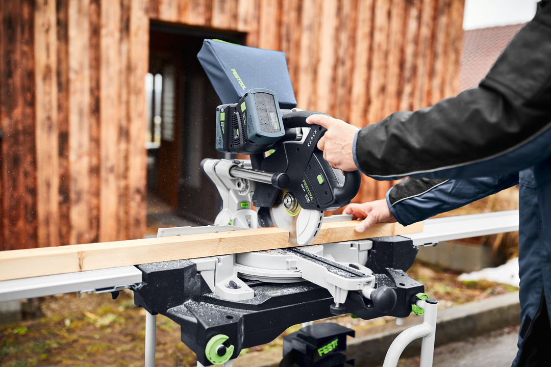 Person using a Festool cordless compound miter saw to cut wood outdoors, part of a woodworking power tools set