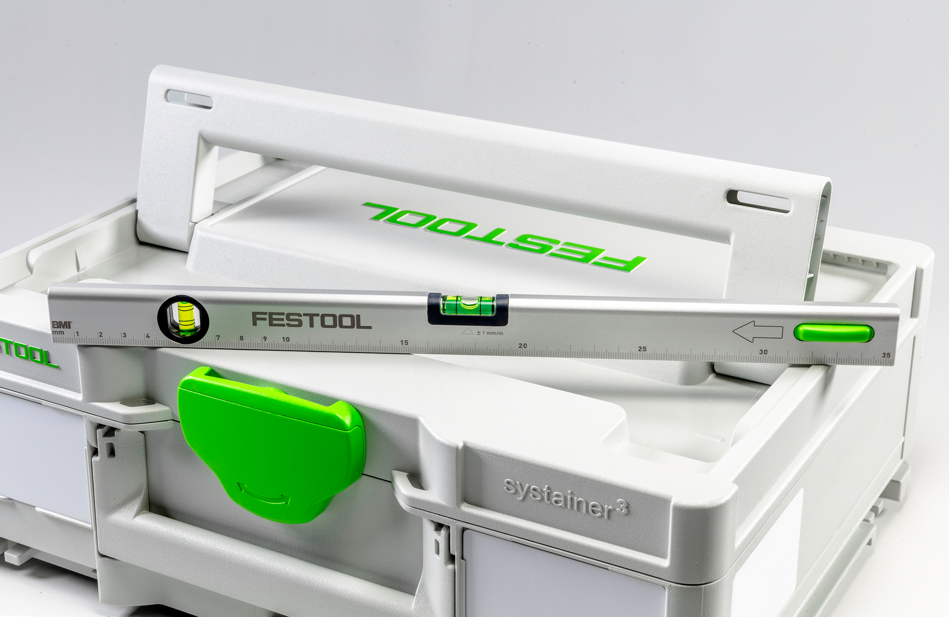 Silver aluminum level with green accents resting on white plastic systainer case for tools and home improvement use