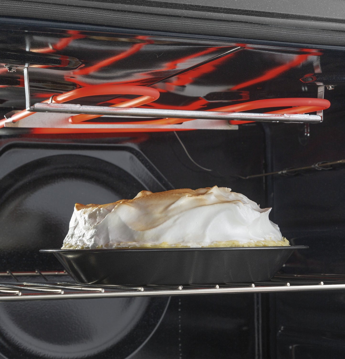Inside view of a range oven with a pie topped with toasted meringue baking beneath the heating element in a kitchen appliance setting