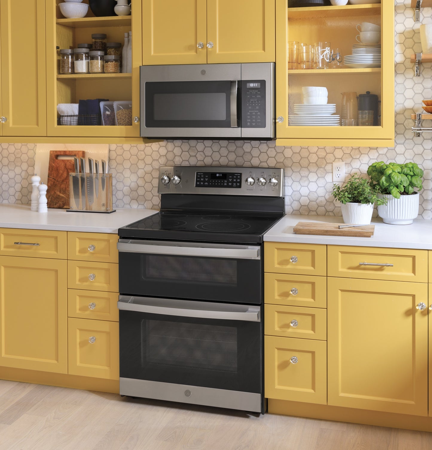 Stainless steel over-the-range microwave above double oven in bright yellow kitchen with white countertop and backsplash tiles