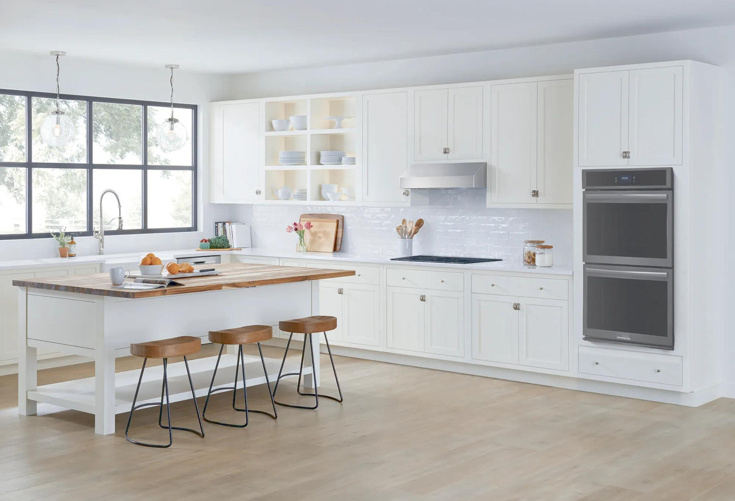 Bright kitchen with white cabinetry, large island with wooden countertop, and built-in double electric wall oven in Appliances collection