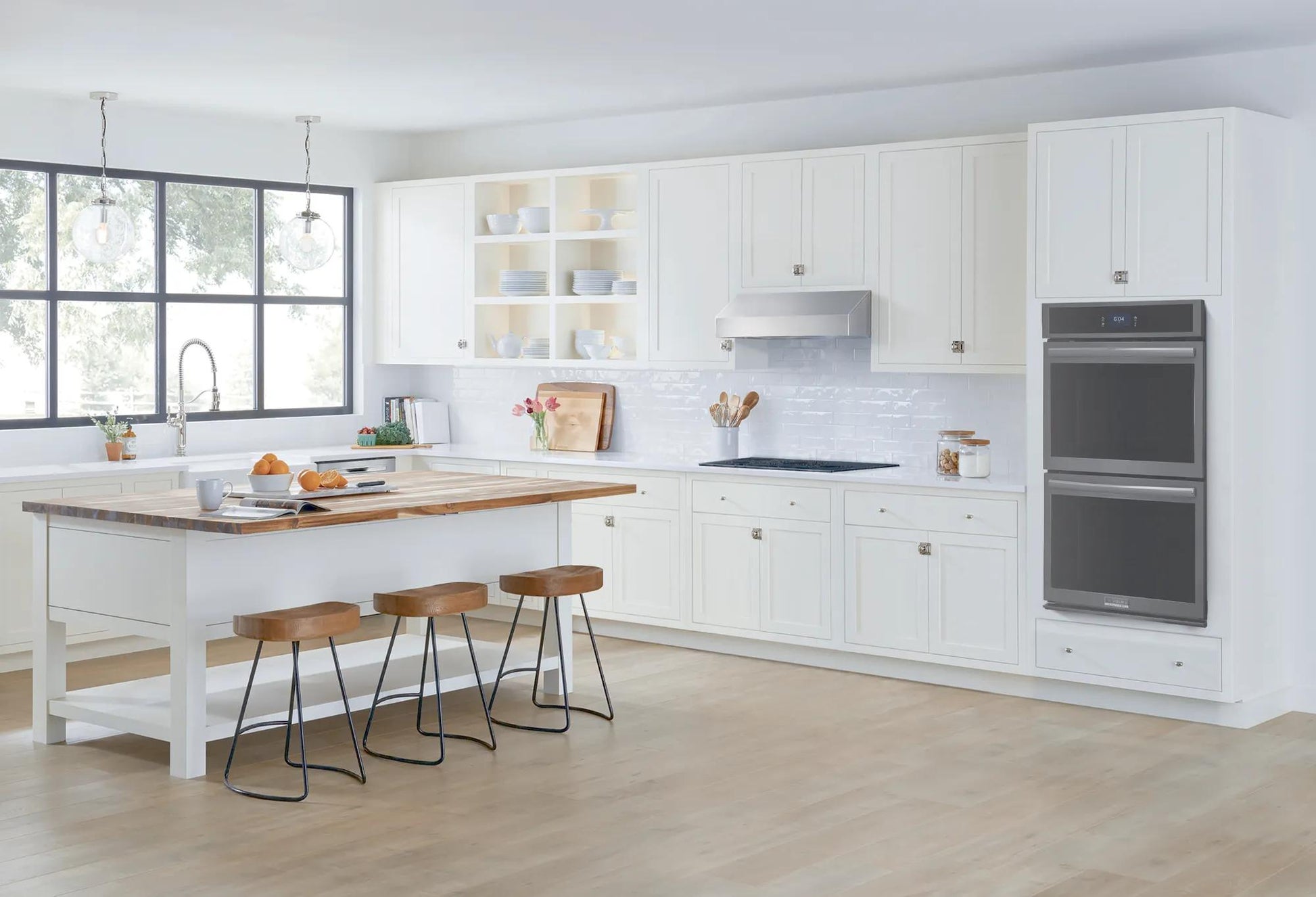 Bright kitchen with white cabinetry, large island with wooden countertop, and built-in double electric wall oven in Appliances collection