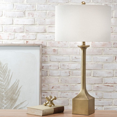 Gold resin table lamp with white drum shade on wooden surface for home improvement decor