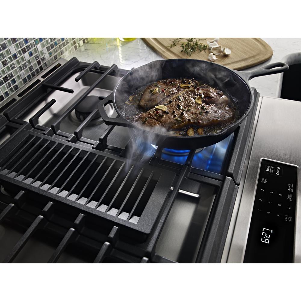 Gas cooktop with four burners and cast iron grill, cooking steak in cast iron skillet, stainless steel slide-in range