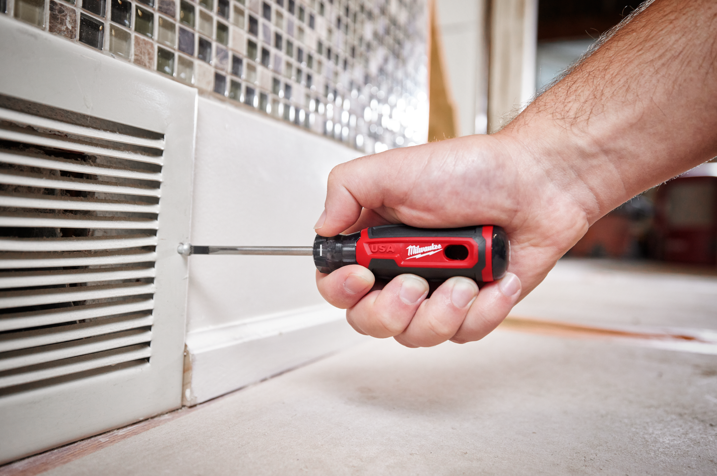 Hand using red and black screwdriver with cushioned grip to tighten vent screws for home improvement use