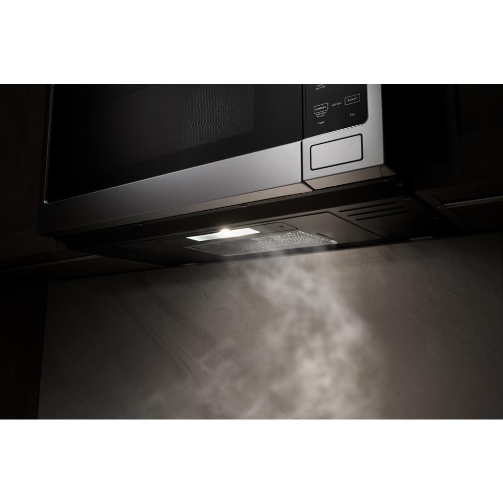 Stainless steel over-the-range microwave with illuminated vent hood releasing steam in kitchen setting