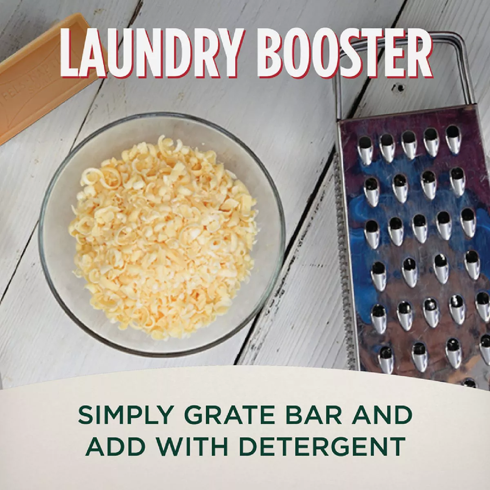 Grated laundry soap shavings in clear bowl next to metal grater on white wooden surface with text overlay