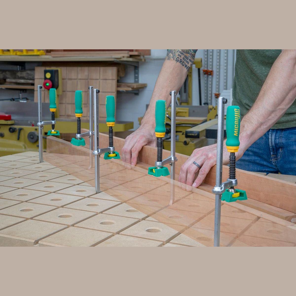 Green-handled dovetail clamps securing wooden boards on a perforated workbench for woodworking assembly tasks