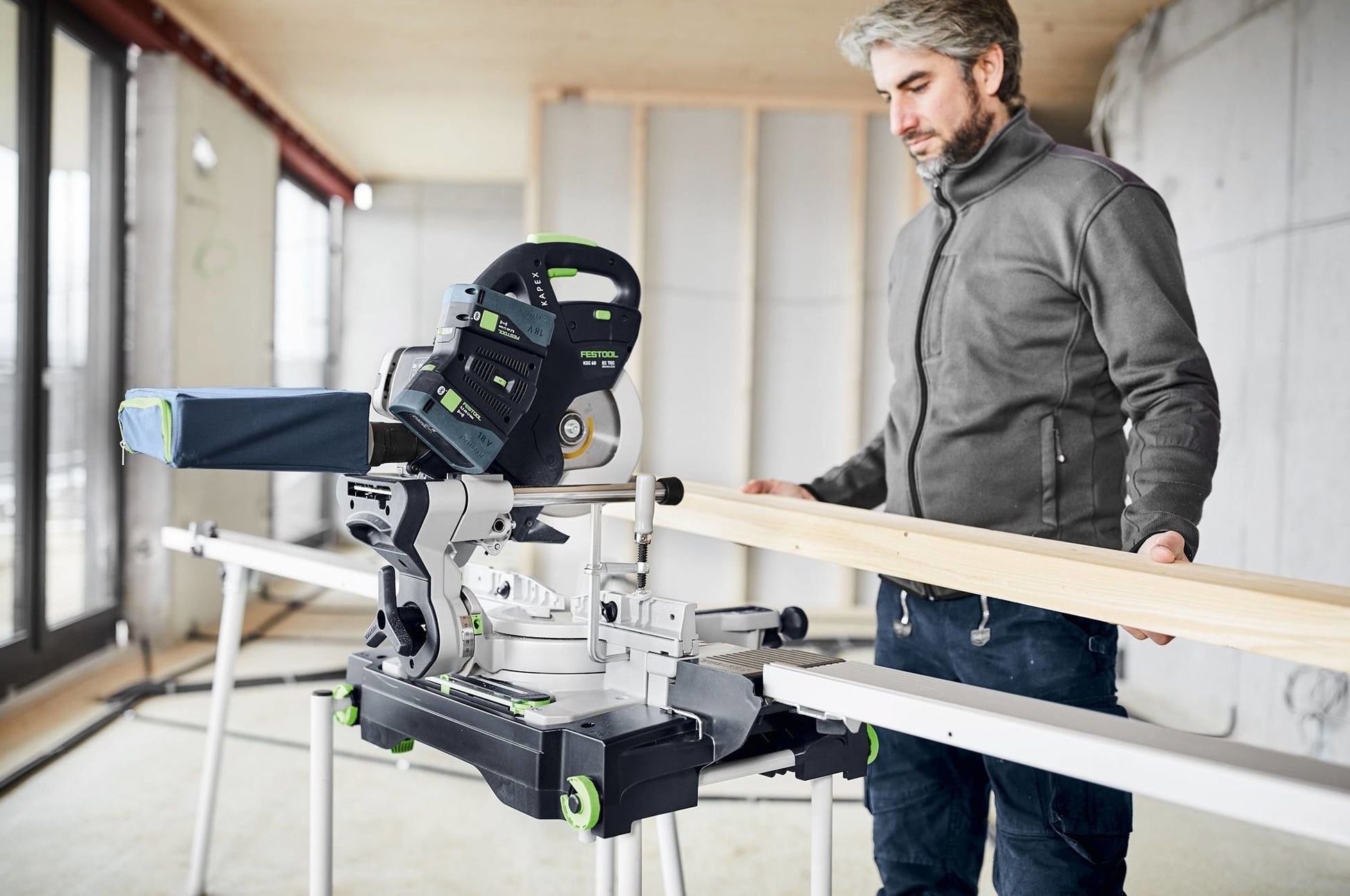 Man preparing to cut wood with cordless sliding compound miter saw in unfinished room, part of power tools collection