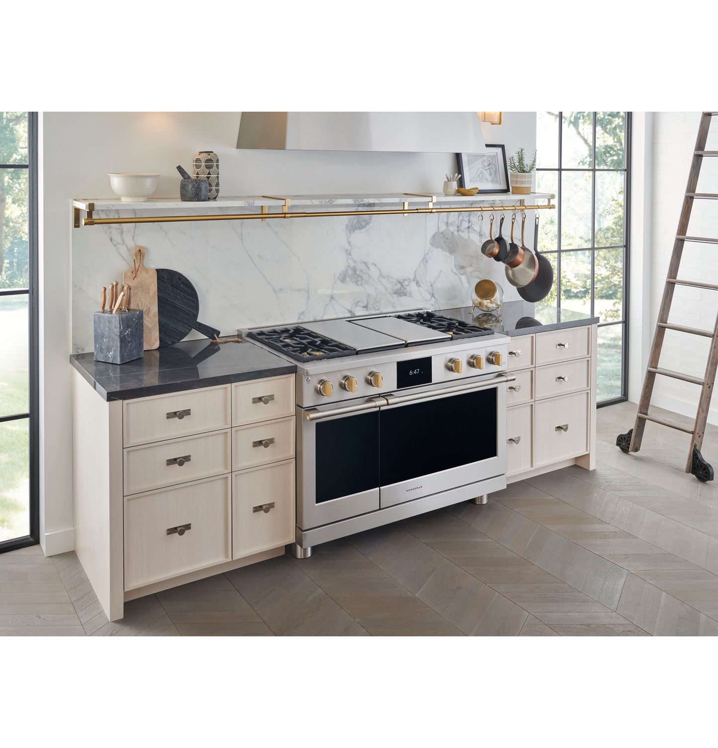 Modern kitchen with stainless steel range hood, light cabinetry, black countertop, and marble backsplash in cooking space