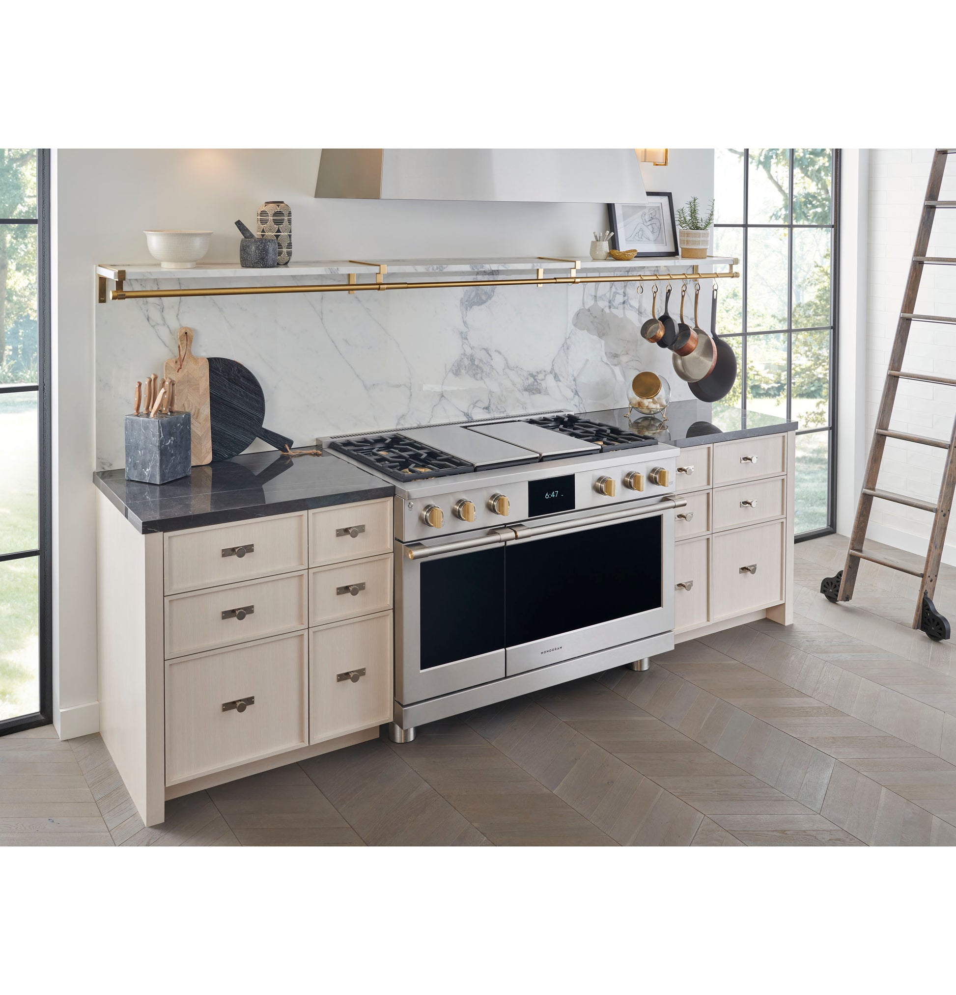 Modern kitchen with stainless steel range hood, light cabinetry, black countertop, and marble backsplash in cooking space