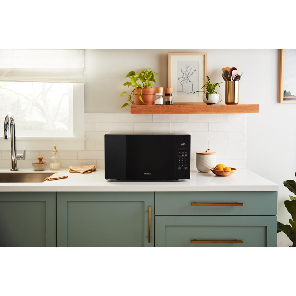 Modern black microwave with digital control panel on white countertop in kitchen with green cabinets and decor