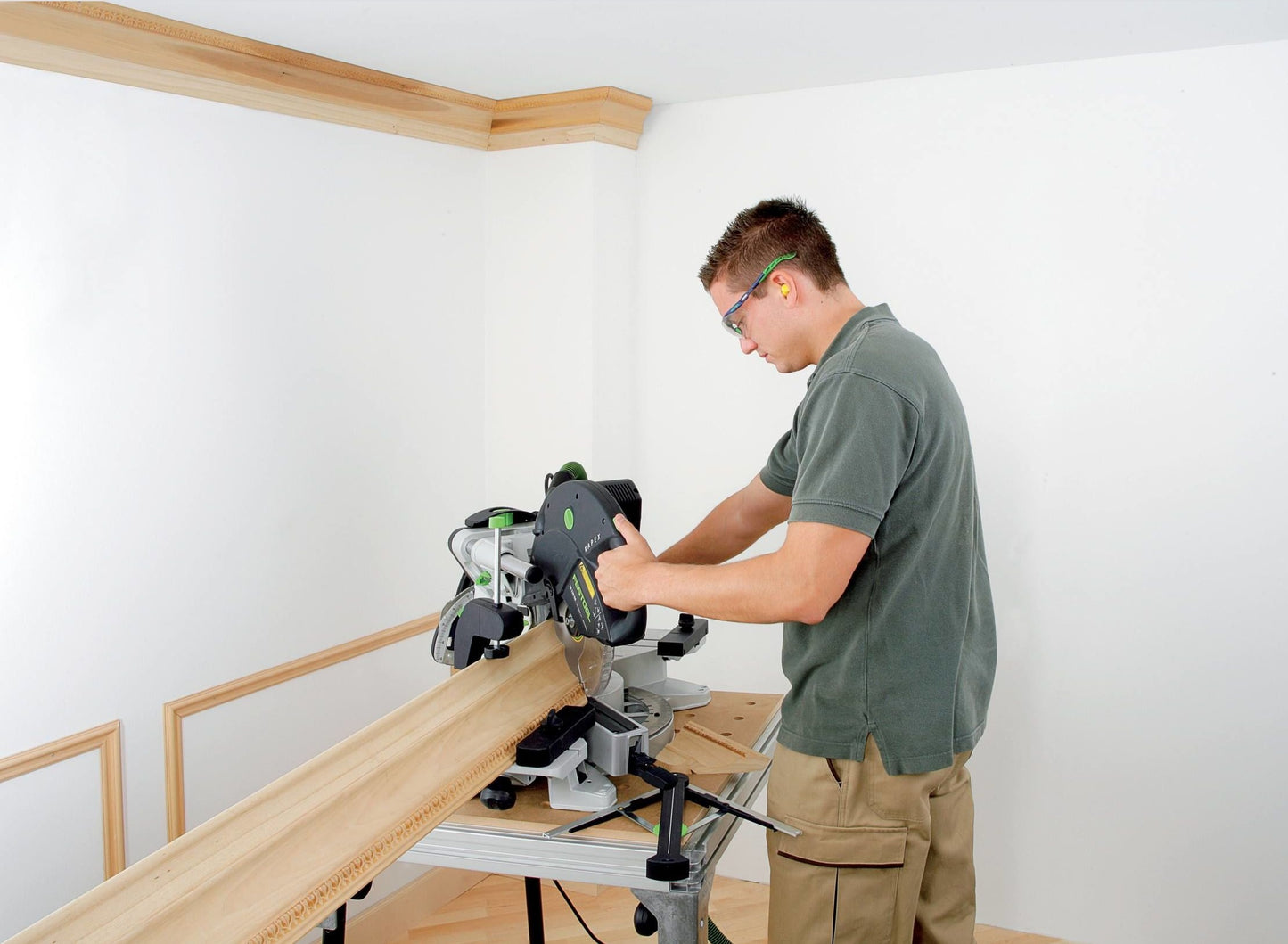 Man using sliding compound miter saw to cut decorative wood trim in a bright workshop from Power Tools collection