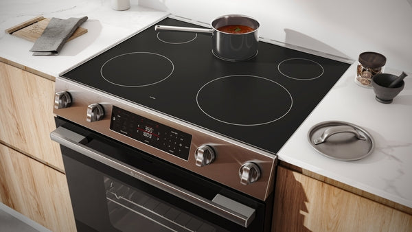 Electric freestanding stainless steel range with smooth black cooktop and saucepan cooking in modern kitchen setting