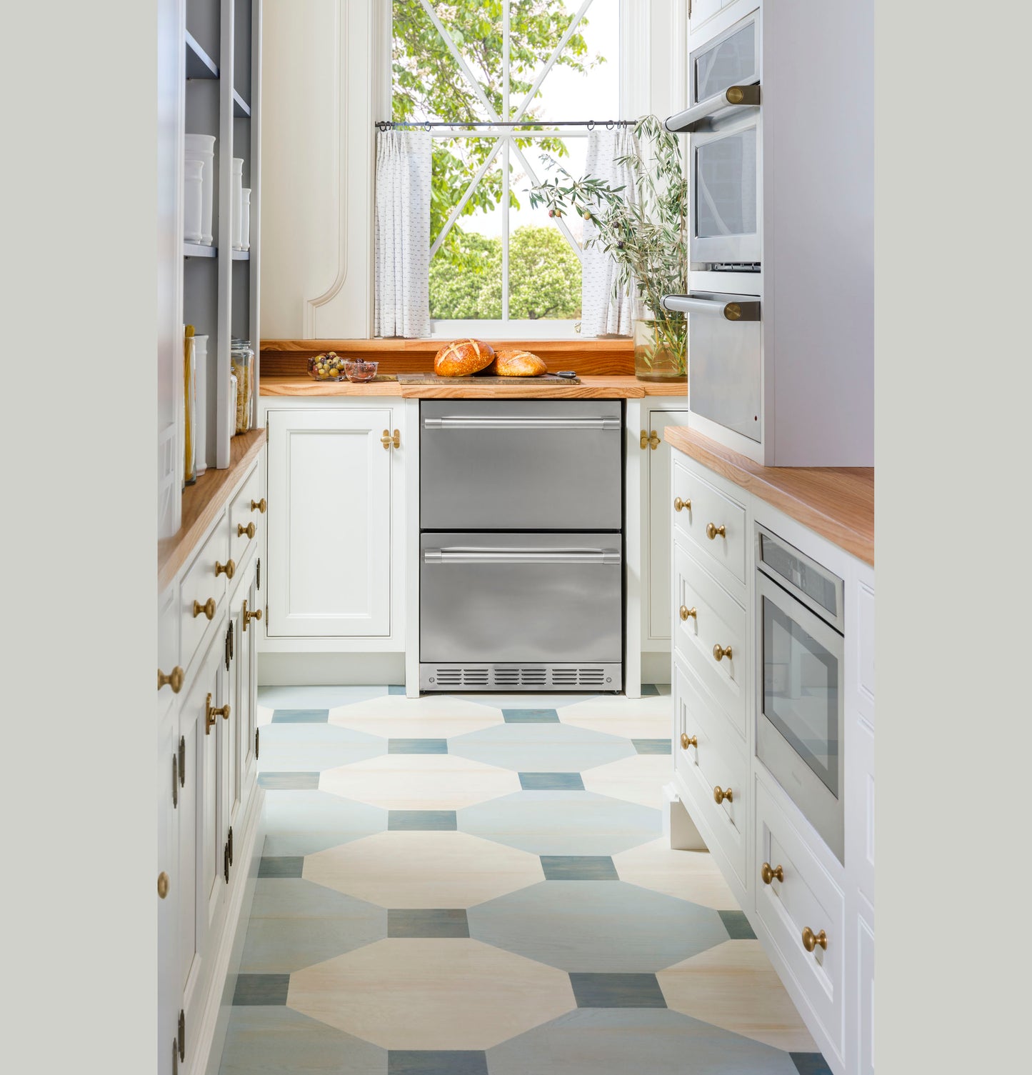 Built-in stainless steel warming drawer integrated into white cabinetry in a bright kitchen with wood countertops.