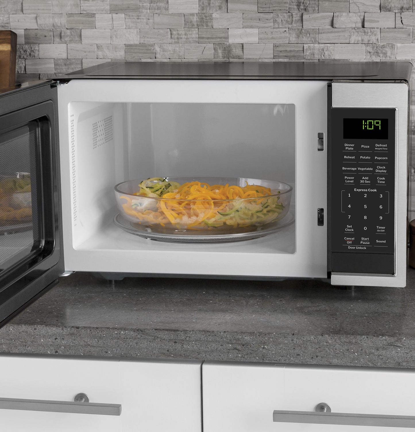 Countertop microwave oven with digital control panel heating a bowl of spiralized vegetables on kitchen countertop