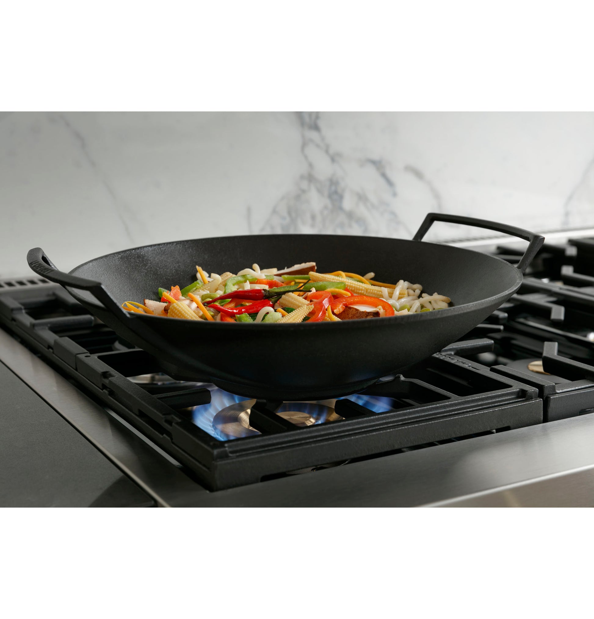 Cast iron wok on stainless steel gas cooktop burner with colorful vegetables cooking in kitchen setting