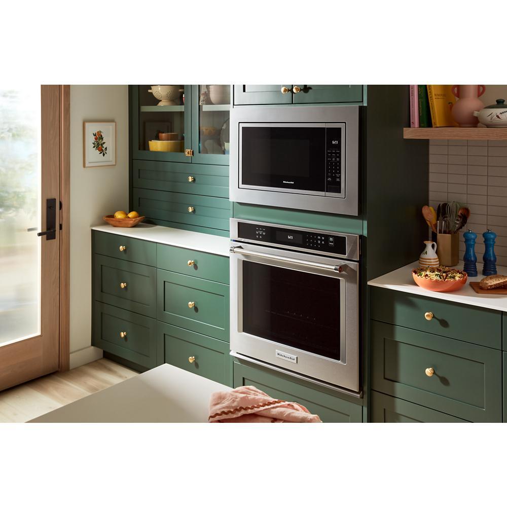 Built-in stainless steel microwave and oven combo integrated into green cabinetry with brass hardware in modern kitchen