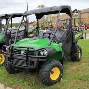 Green and yellow John Deere utility vehicle with off-road tires and protective roof for outdoor work tasks