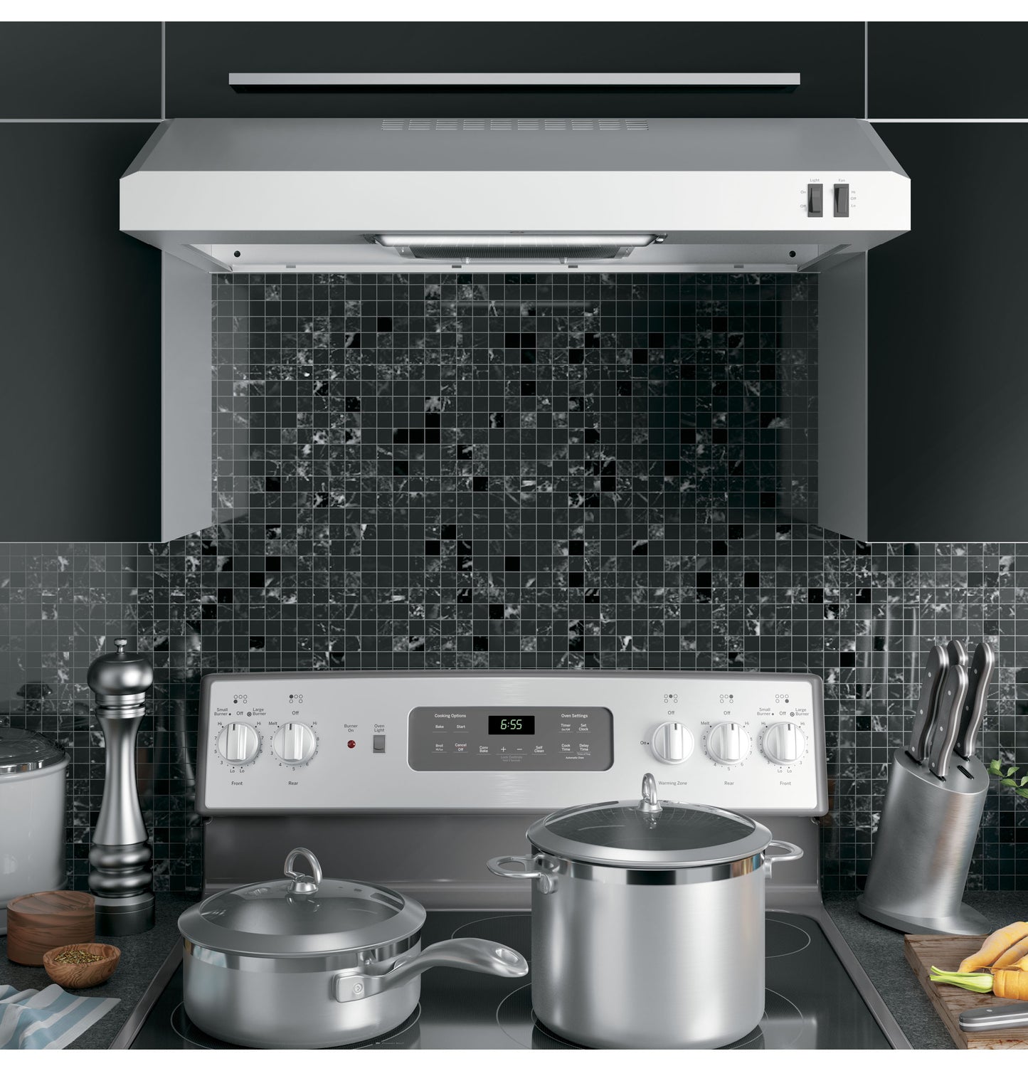 Under the cabinet stainless steel range hood above stove with cookware, knife block, and black tile backsplash in kitchen