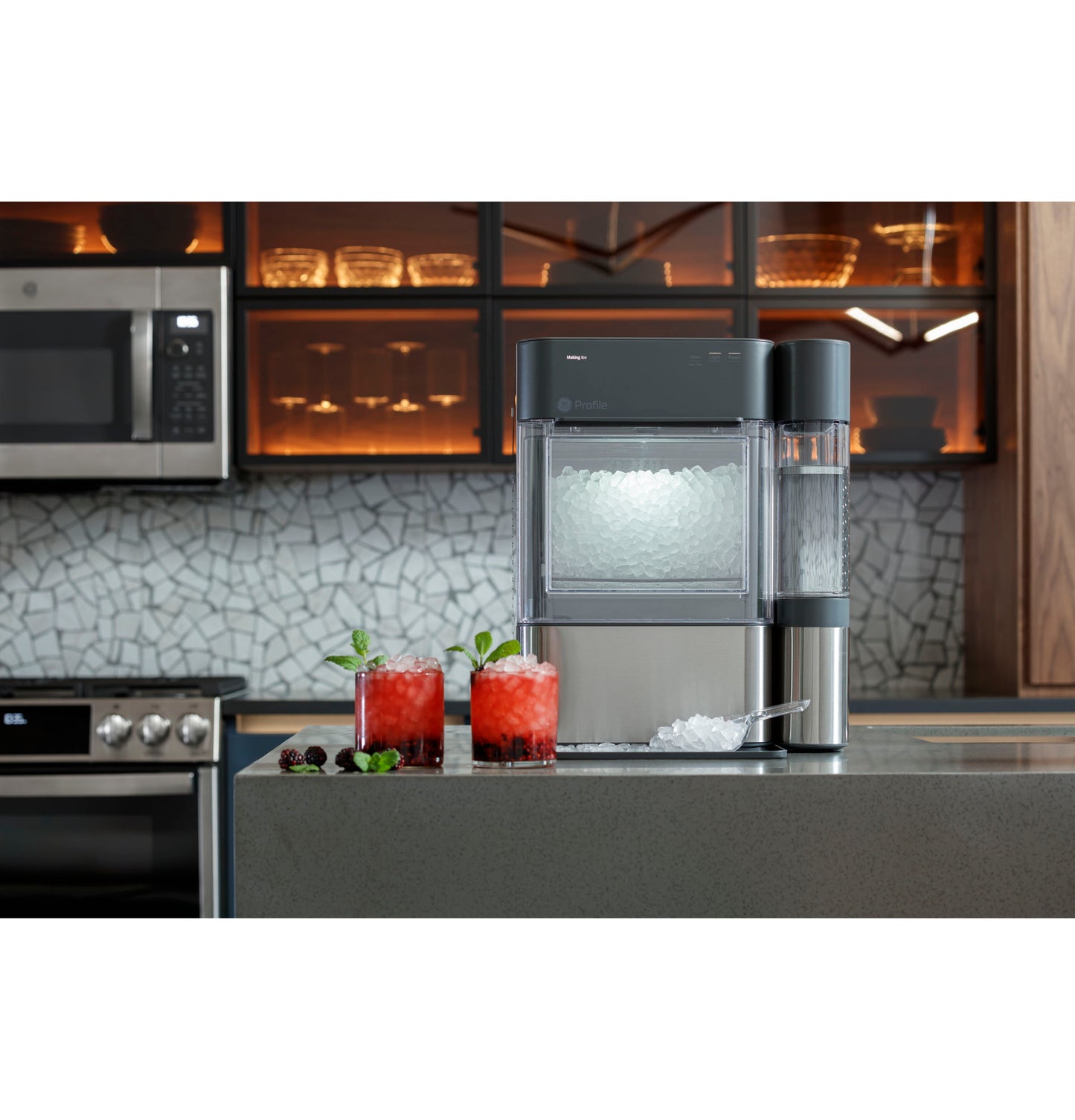 Modern ice maker with built-in dispenser on kitchen countertop near red cocktails and stainless steel appliances