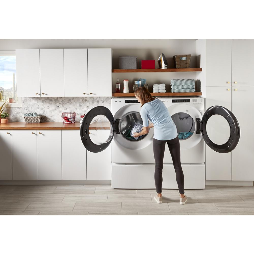 Woman loading a front load washer and dryer elevated on white pedestals in a modern laundry room setting