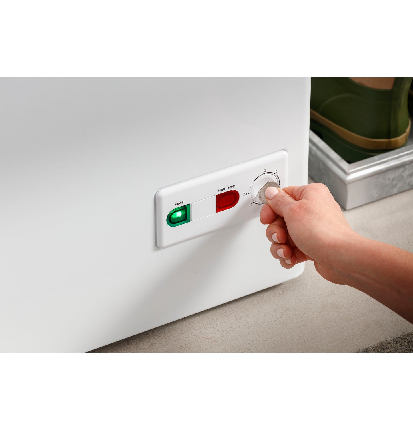 Close-up of hand adjusting temperature dial on white chest freezer with power and high temperature indicator lights in appliance setting