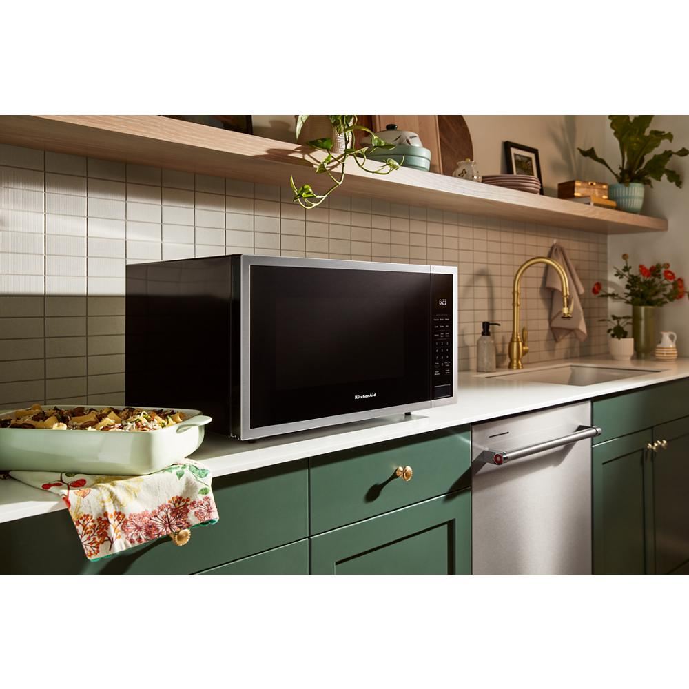 Black KitchenAid microwave with digital control panel on countertop in green and stainless steel kitchen setting