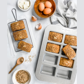 Non-stick 8 well mini loaf pan with freshly baked loaves, styled with eggs, oats, and kitchenware for baking collections under $50