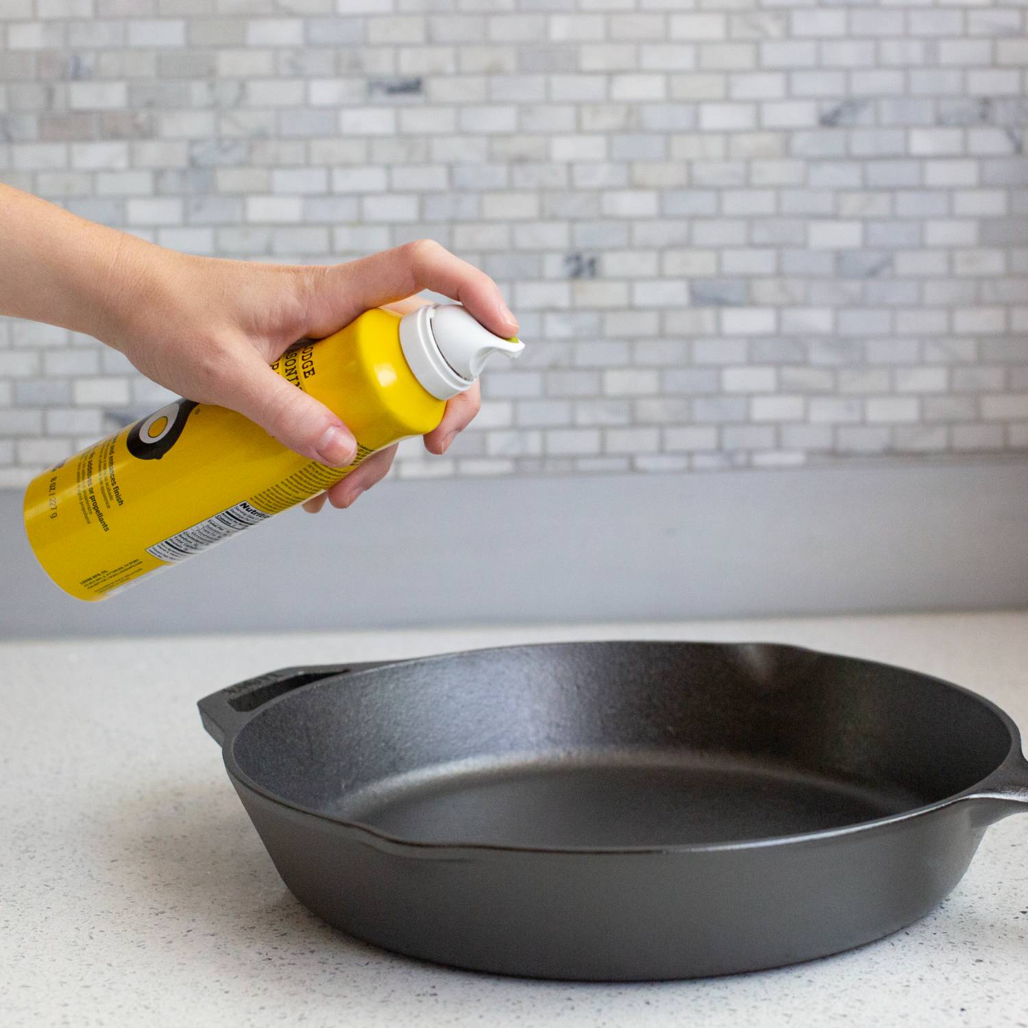 Yellow seasoning spray can being applied to black cast iron skillet on kitchen counter in Kitchenware collection