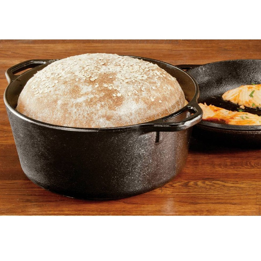 Black cast iron Dutch oven filled with rising bread dough alongside cast iron skillet with cooked food in kitchenware collection