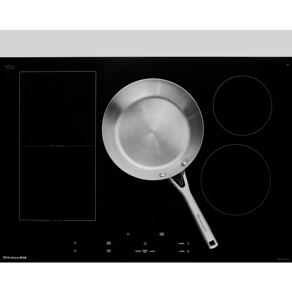 Black glass induction cooktop with five cooking zones and stainless steel skillet from KitchenAid appliances collection