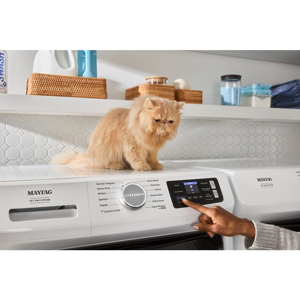 Person using touchscreen controls on white front load washer with pet sitting on top in laundry room setting