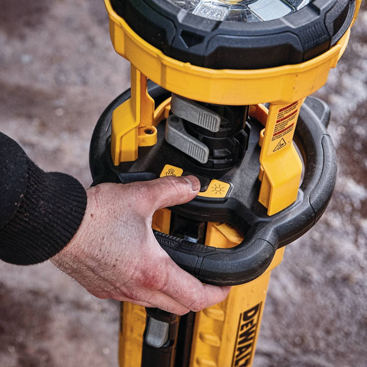 Hand pressing power button on yellow DEWALT cordless tripod work light for tool accessories use