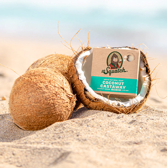 Dr. Squatch Coconut Castaway soap bar nestled inside a coconut shell on sandy beach background