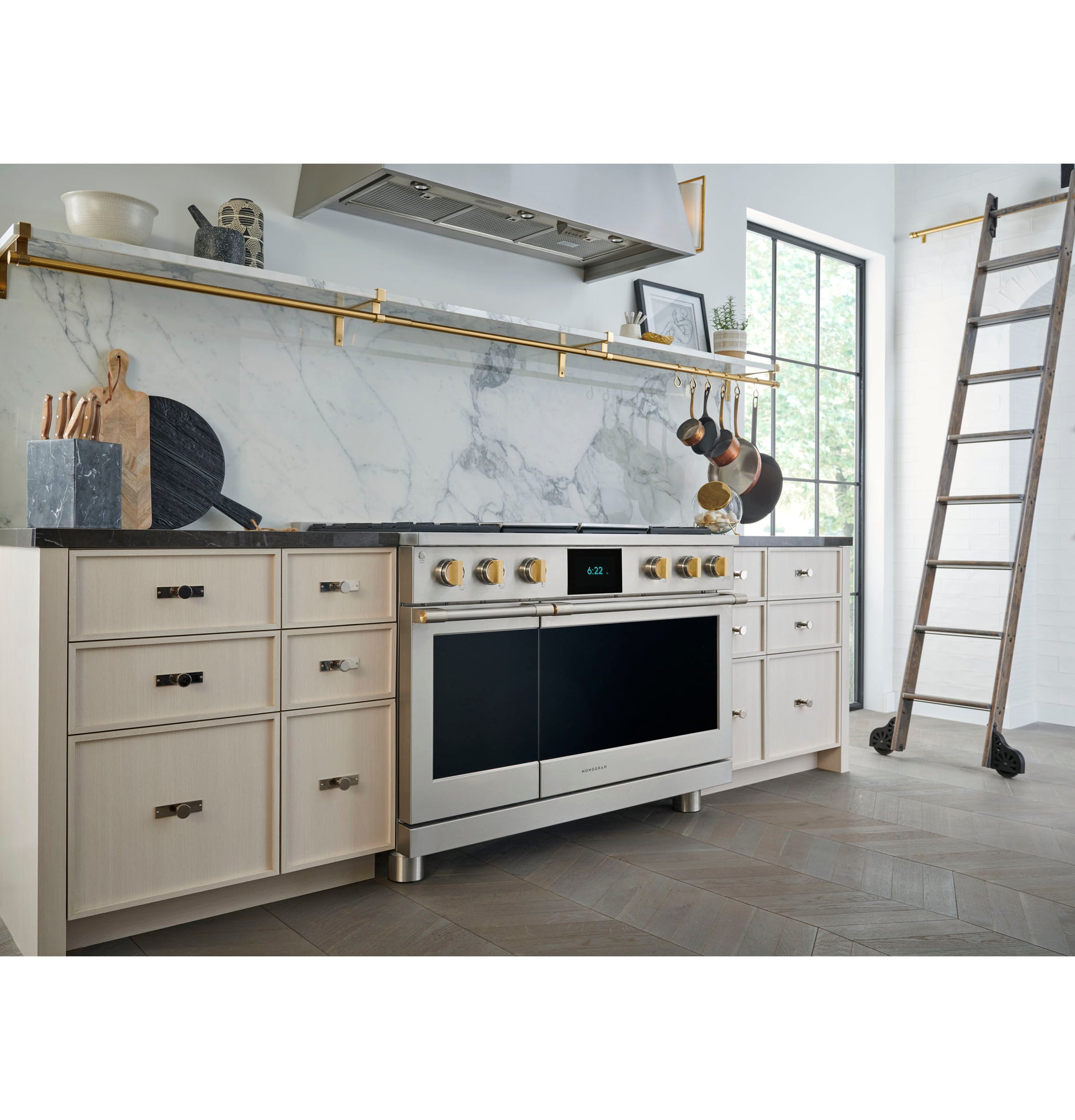 Sleek stainless steel range hood above contemporary stove with light wood cabinets and marble backsplash in kitchenware collection