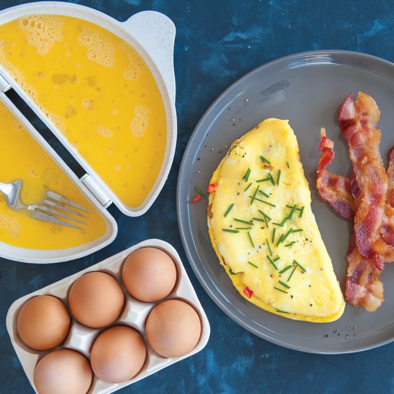 White divided omelet pan with raw beaten eggs, cooked folded omelet garnished with chives, and crispy bacon strips on plate