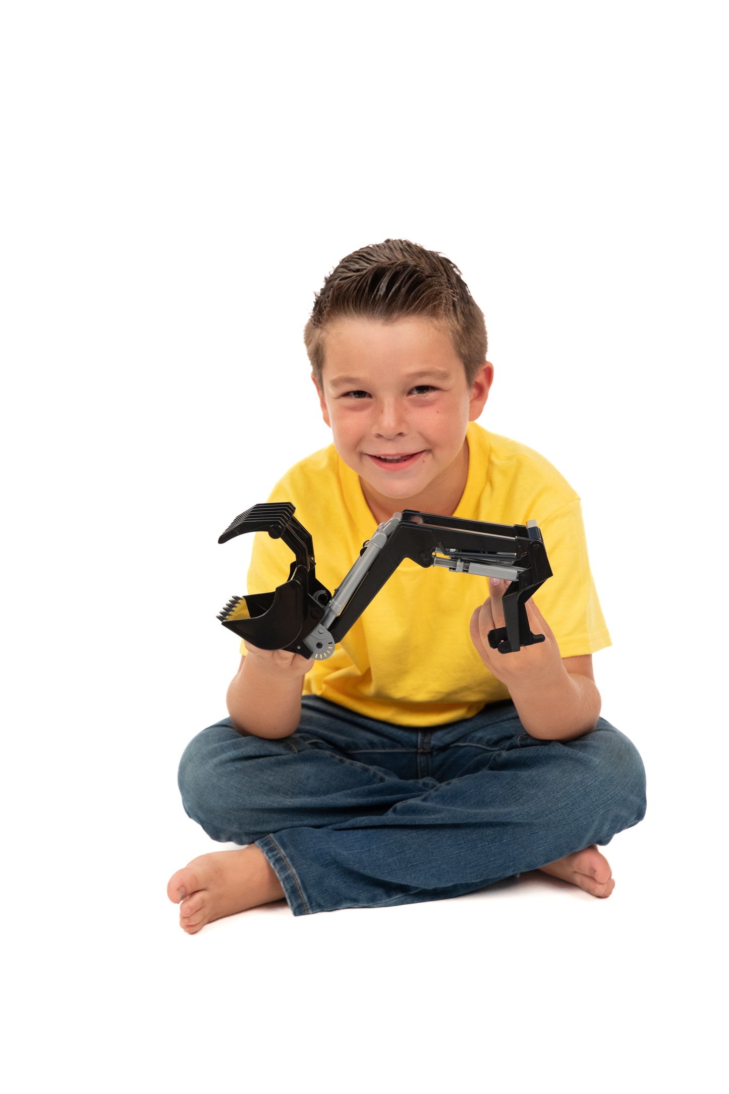 Young boy sitting cross-legged holding black plastic front loader toy attachment for tractor in home play setting